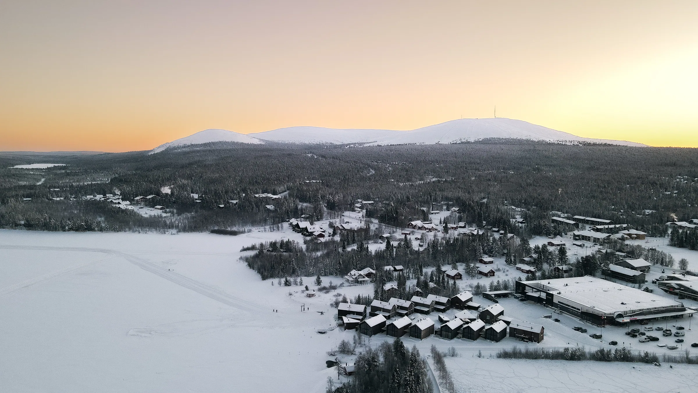 Ilmakuva lomakylästä ja tuntureista pehmeässä auringonlaskun valossa