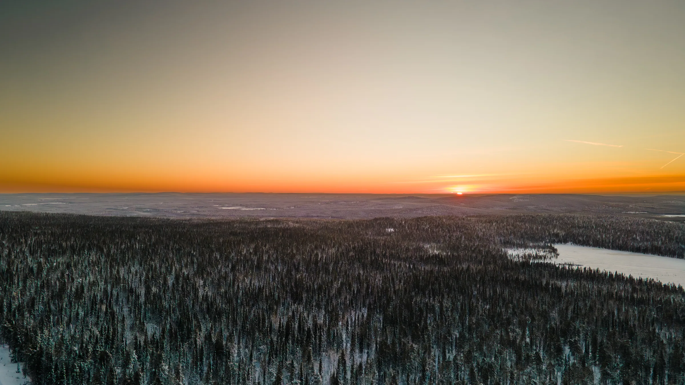 Ilmakuva lumisesta metsästä ja lomakylästä auringonlaskun aikaan Lapissa