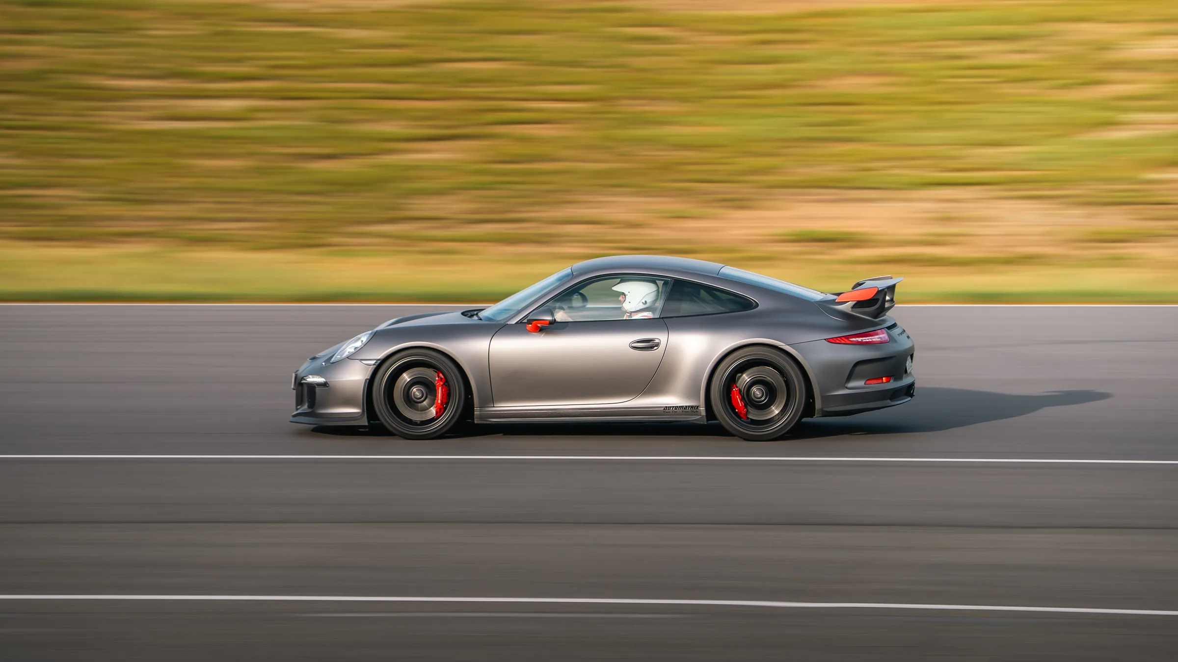 Harmaa Porsche 911 GT3 kiitää radalla panning-kuvassa tausta liike-epäterävänä, ratapäivä Alastaron radalla