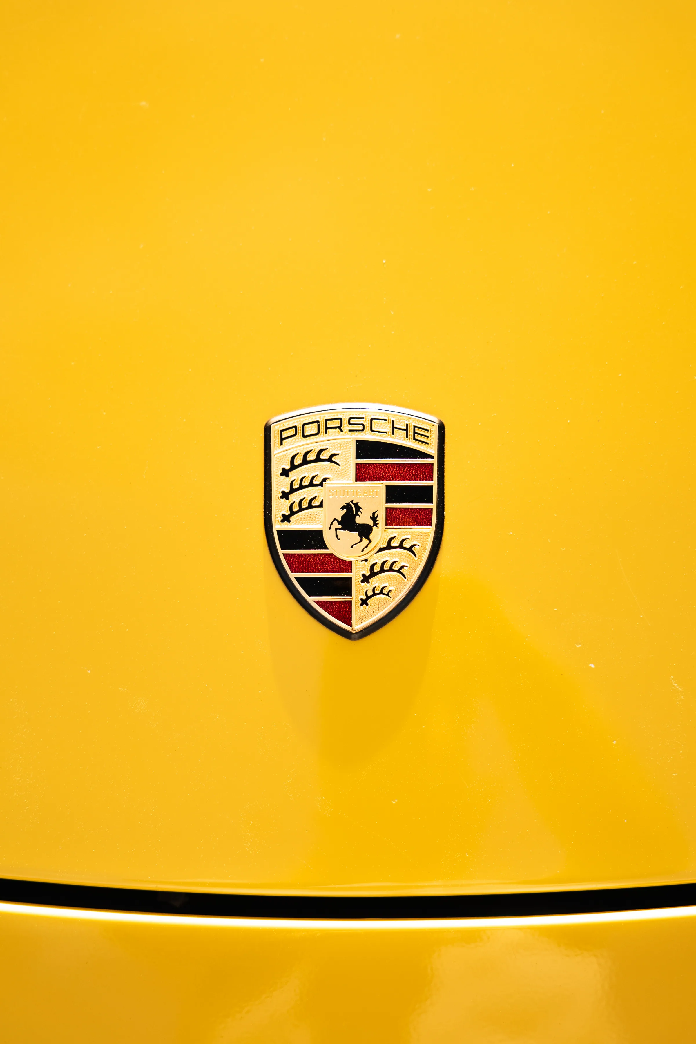 Lähikuva keltaisen urheiluauton kiiltävästä konepellistä ja Porsche-tunnuksesta